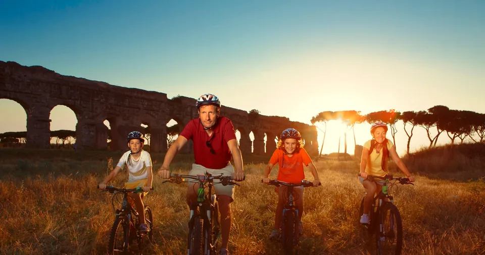 The arches of an ancient aqueduct in the countryside at sunset, with some cyclists backlit