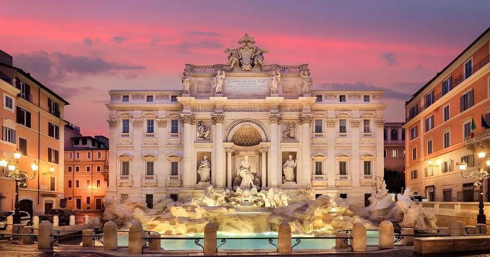 A large Baroque fountain lit at sunset in a square surrounded by palaces